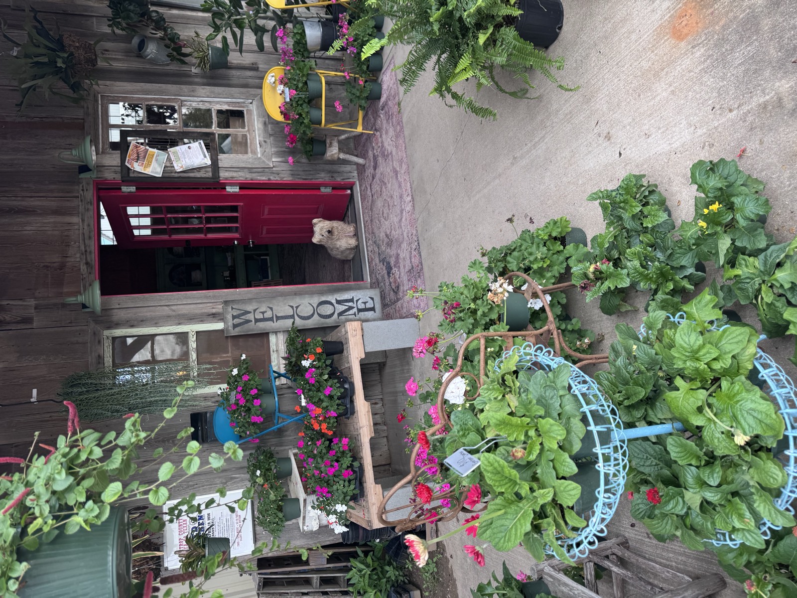 Rustic Welcome storefront at String Prairie Gardens with colorful potted plants and red door
