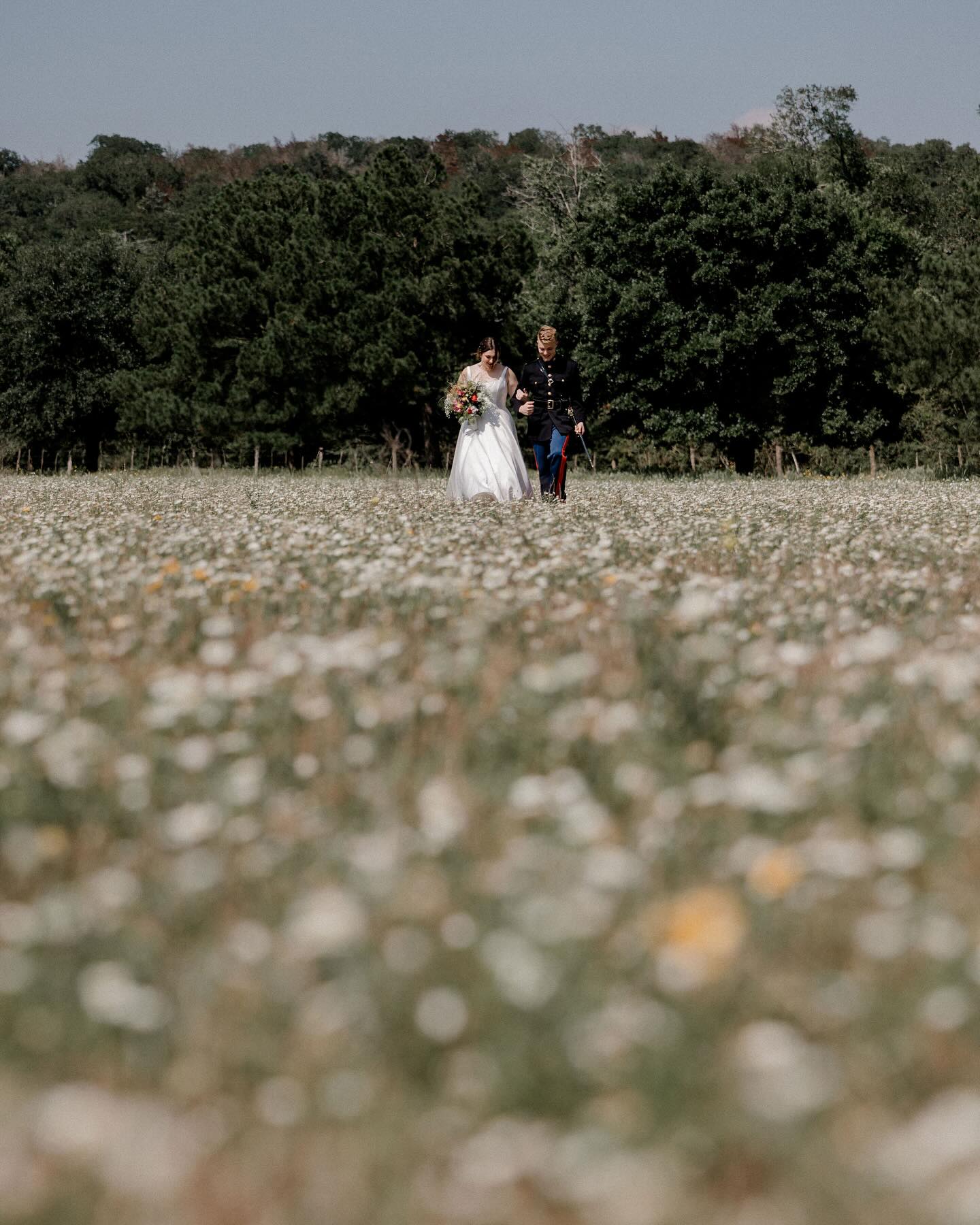 Bride and groom walking through a wildflower field with bouquet