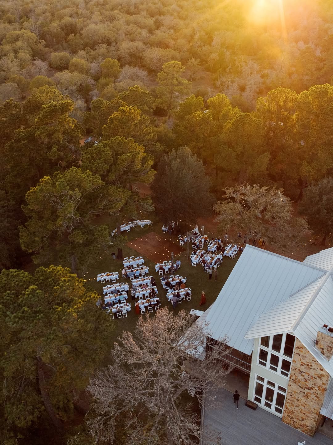 Aerial golden hour view of outdoor wedding reception with string lights and elegant table settings